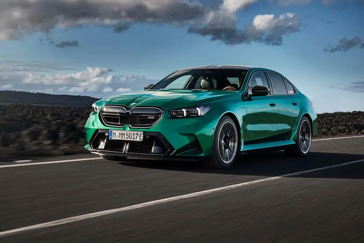 Zielony BMW M5 na drodze, chmury na niebie. Sprawdź aktualną bmw m5 cena i możliwości tego sportowego sedana.