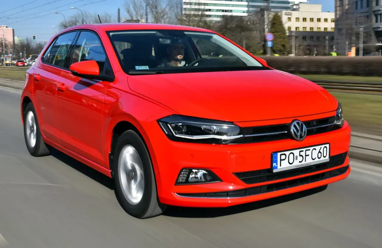Czerwony Volkswagen Polo 6 w ruchu miejskim. Kierowca w okularach przeciwsłonecznych prowadzi auto po ulicy.