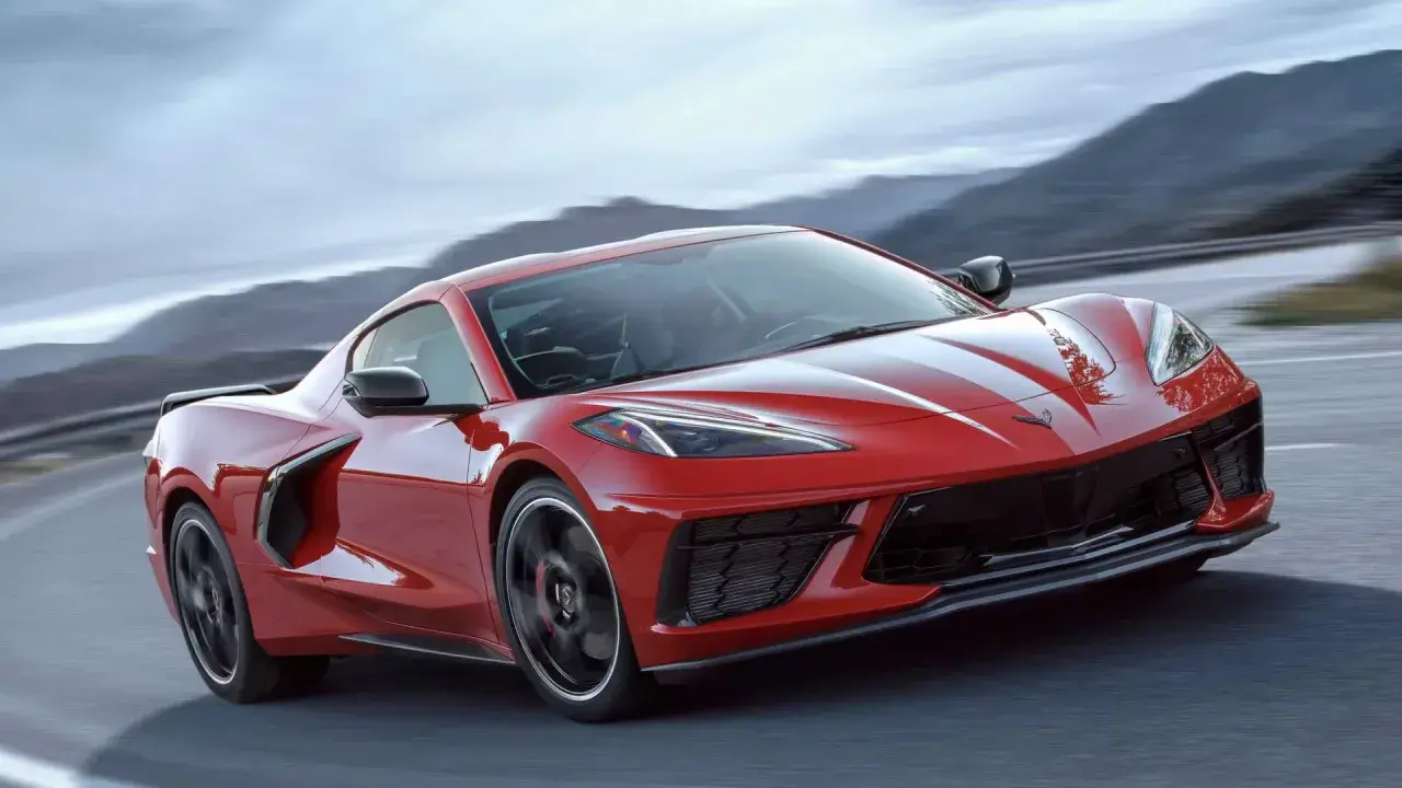 Czerwony Chevrolet Corvette C8 z białymi pasami pędzi po krętej drodze wśród gór.