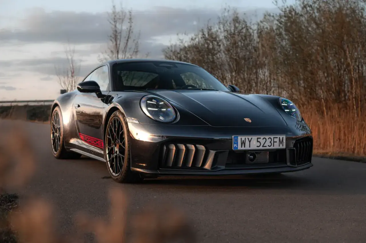 Czarny Porsche GTS z czerwonymi akcentami na progu, zaparkowany na drodze wśród suchych traw.