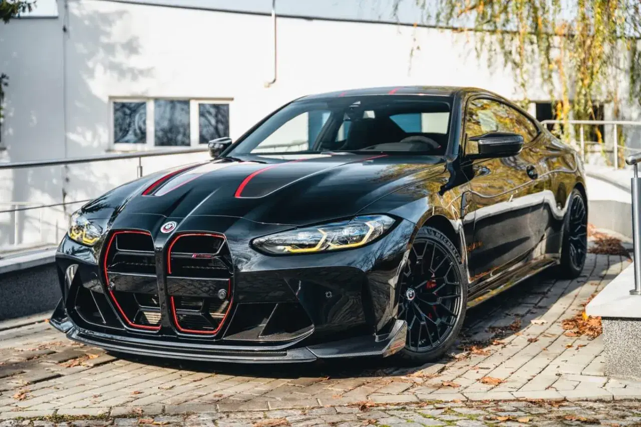 Czarny BMW M4 CSL z czerwonymi akcentami i sportowym dyfuzorem, zaparkowany na bruku.