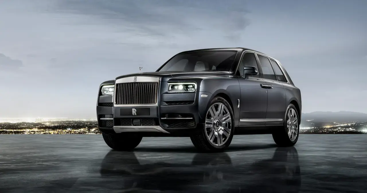 Elegancki Rolls-Royce SUV w ciemnym kolorze, lśniącym na tle nocnego miasta i gór.