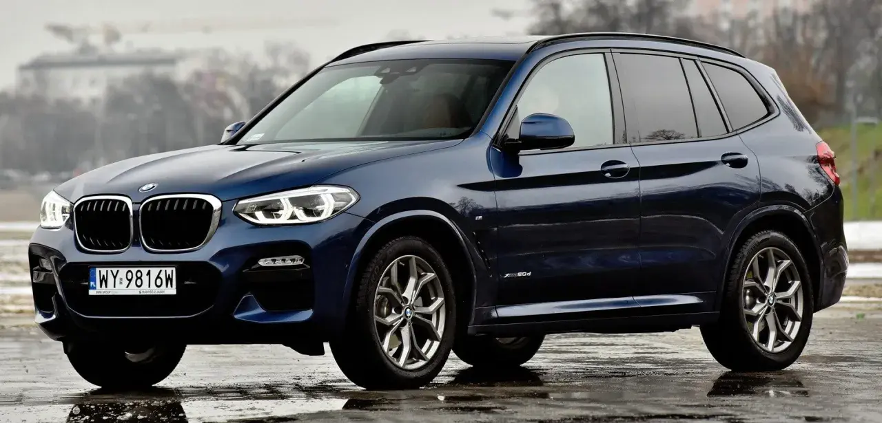 Ciemnoniebieskie BMW X3 na mokrej nawierzchni. Eleganckie linie i sportowy charakter tego SUV-a robią wrażenie.