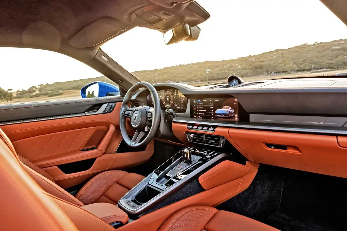 Wnętrze Porsche 911 GTS w kolorze pomarańczowym, z nowoczesnym kokpitem i ekranem multimedialnym.