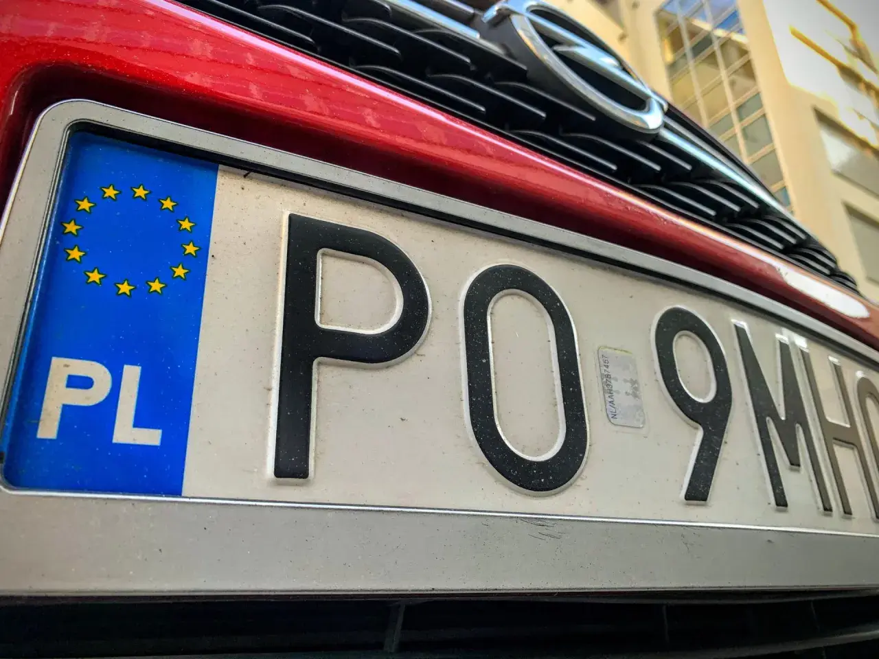 Czerwony samochód z polską tablicą rejestracyjną PO 9MH0. Widoczny fragment grilla i logo marki.