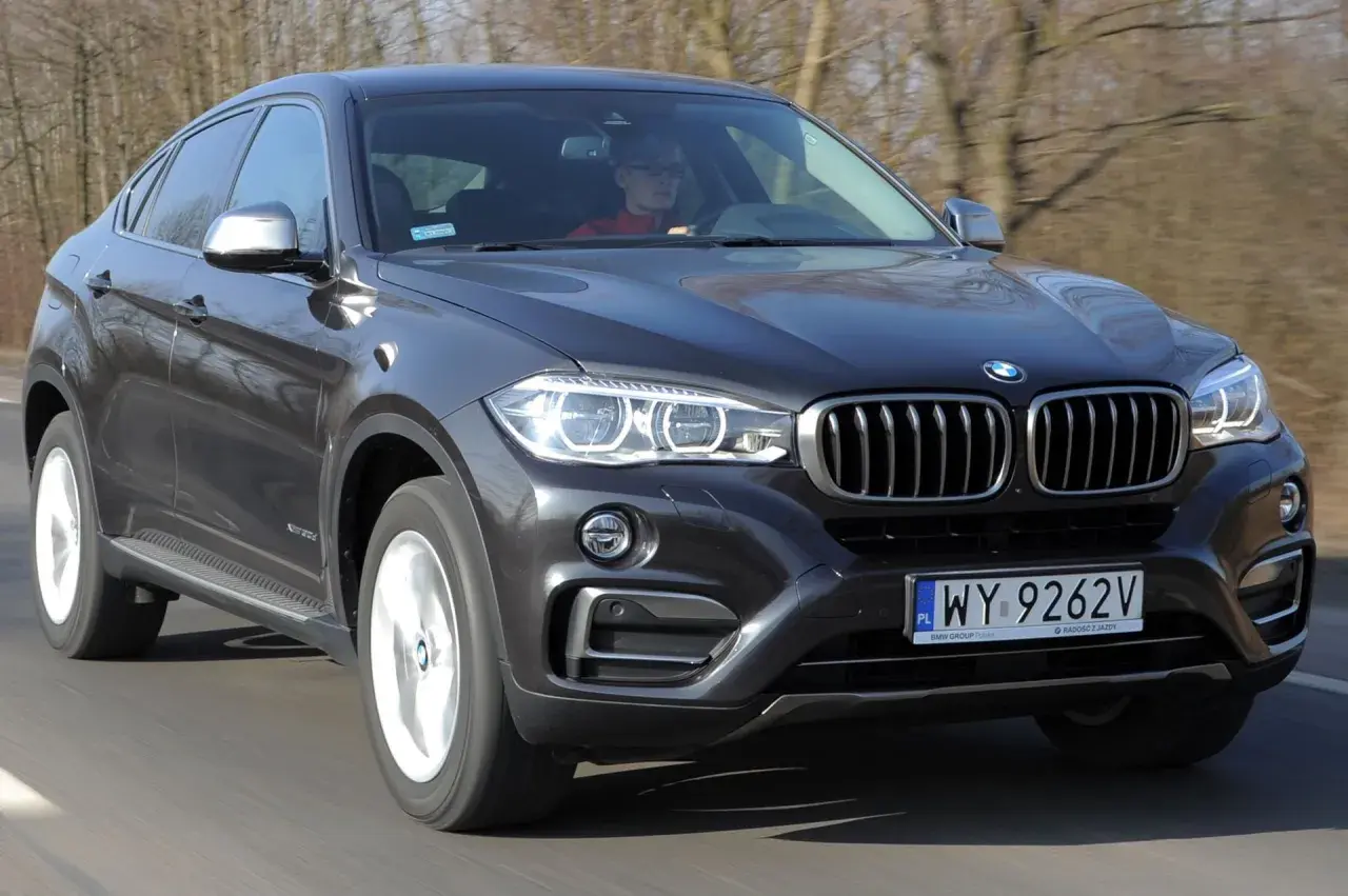 Ciemnoszary BMW F16 w ruchu drogowym, z kierowcą za kierownicą.