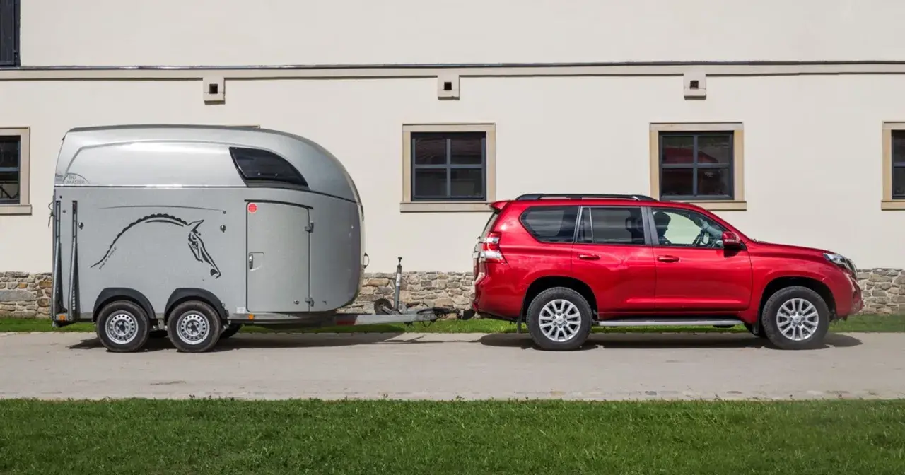 Czerwony SUV holuje przyczepę kempingową z rysunkiem konia. Idealny zestaw dla posiadaczy prawa jazdy na przyczepę.
