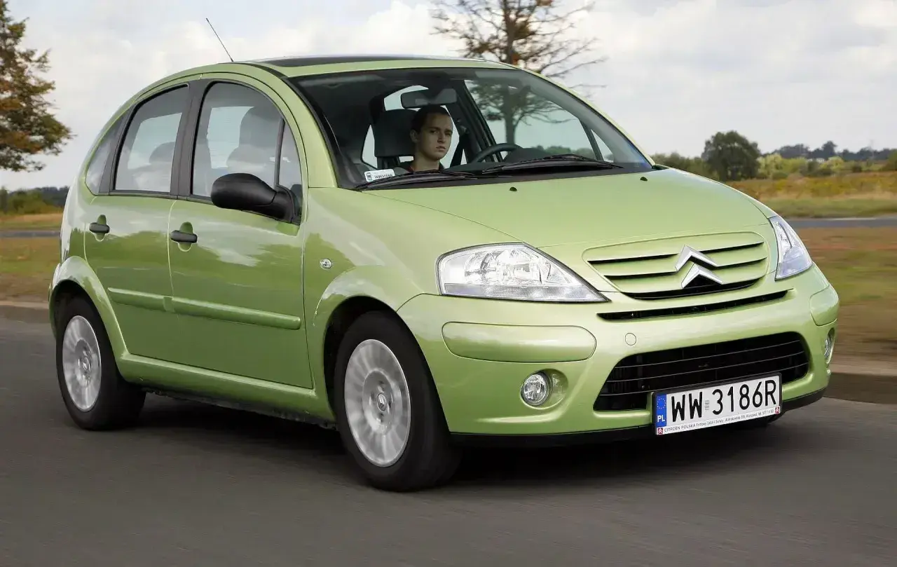 Zielony Citroen C3 z 2003 roku jedzie po drodze. Za kierownicą siedzi młody mężczyzna.