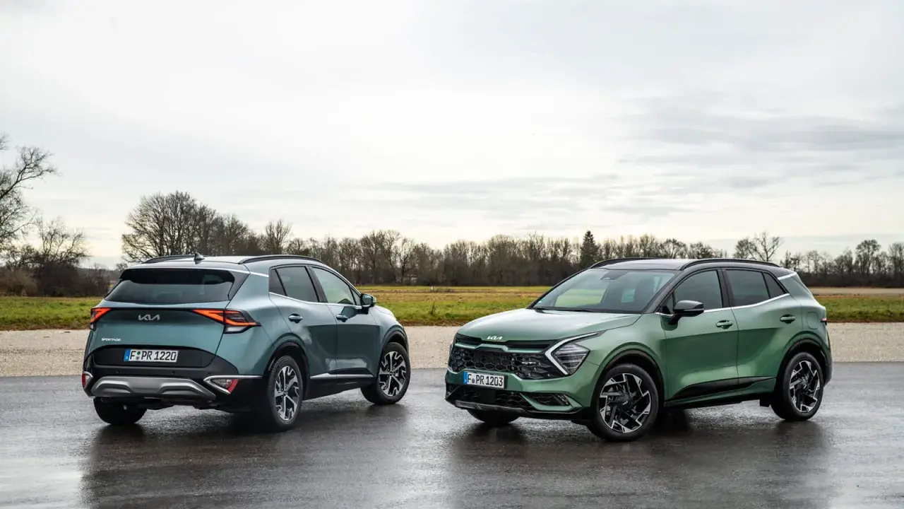 Dwa nowe Kia Sportage GT Line w zielonych odcieniach stoją na mokrej drodze.