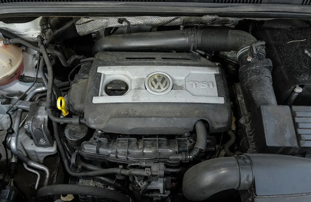 Silnik 2.0 TSI Volkswagena, widok z góry. Widać pokrywę silnika z logo VW i napisem TSI, elementy układu dolotowego i chłodzenia.
