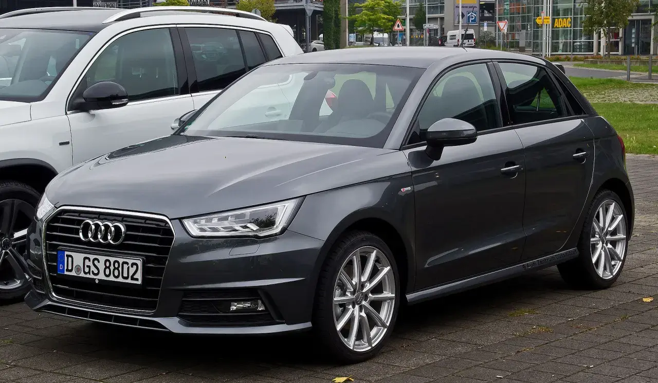 Ciemnoszary Audi 1 z niemieckimi tablicami rejestracyjnymi D.GS 8802 stoi obok białego SUV-a.