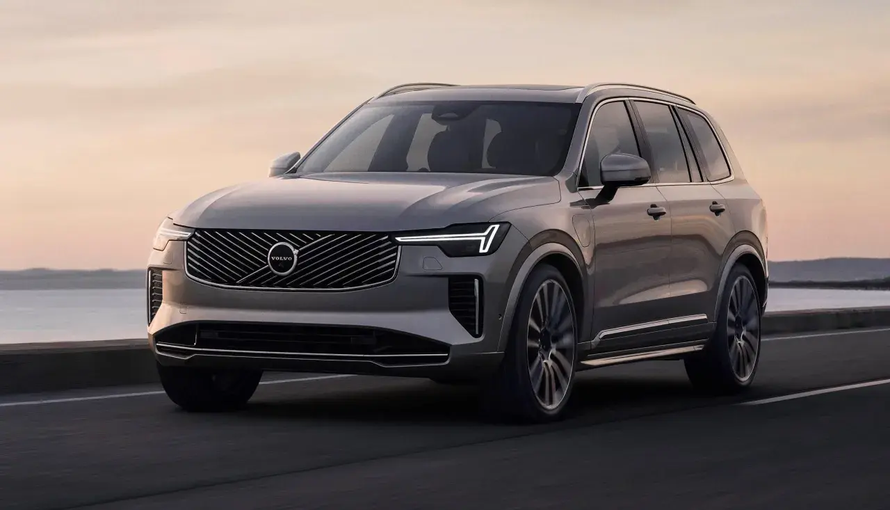 Elegancki, szary Volvo CX90 jedzie po drodze nad morzem o zachodzie słońca.