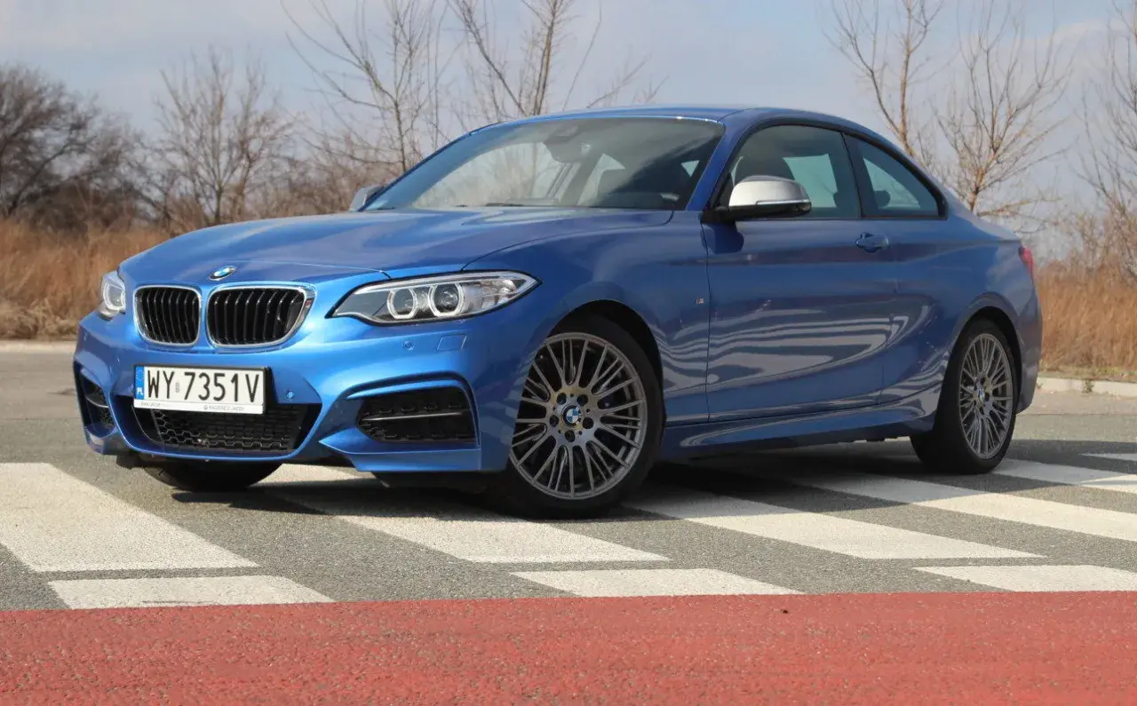 Niebieskie BMW 235i na pasach. Sportowy samochód z charakterystycznym grillem i felgami.