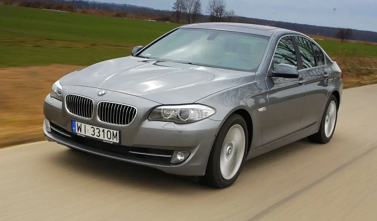 Szare BMW 535d w ruchu, z widokiem na przednią część samochodu i krajobraz.