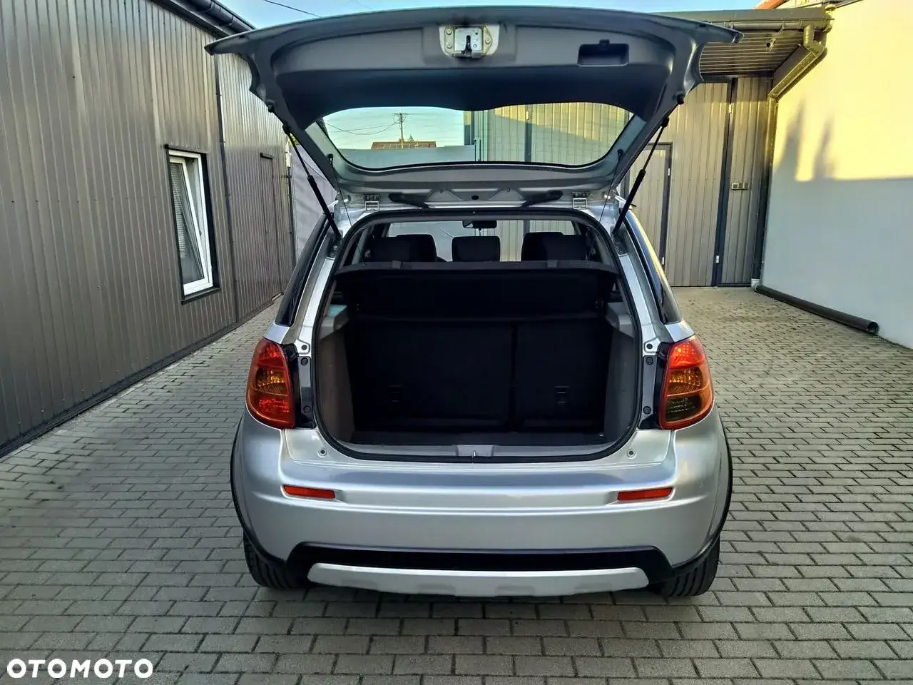 Srebrny Suzuki SX4 1.6 benzyna z otwartym bagażnikiem, gotowy na podróż.