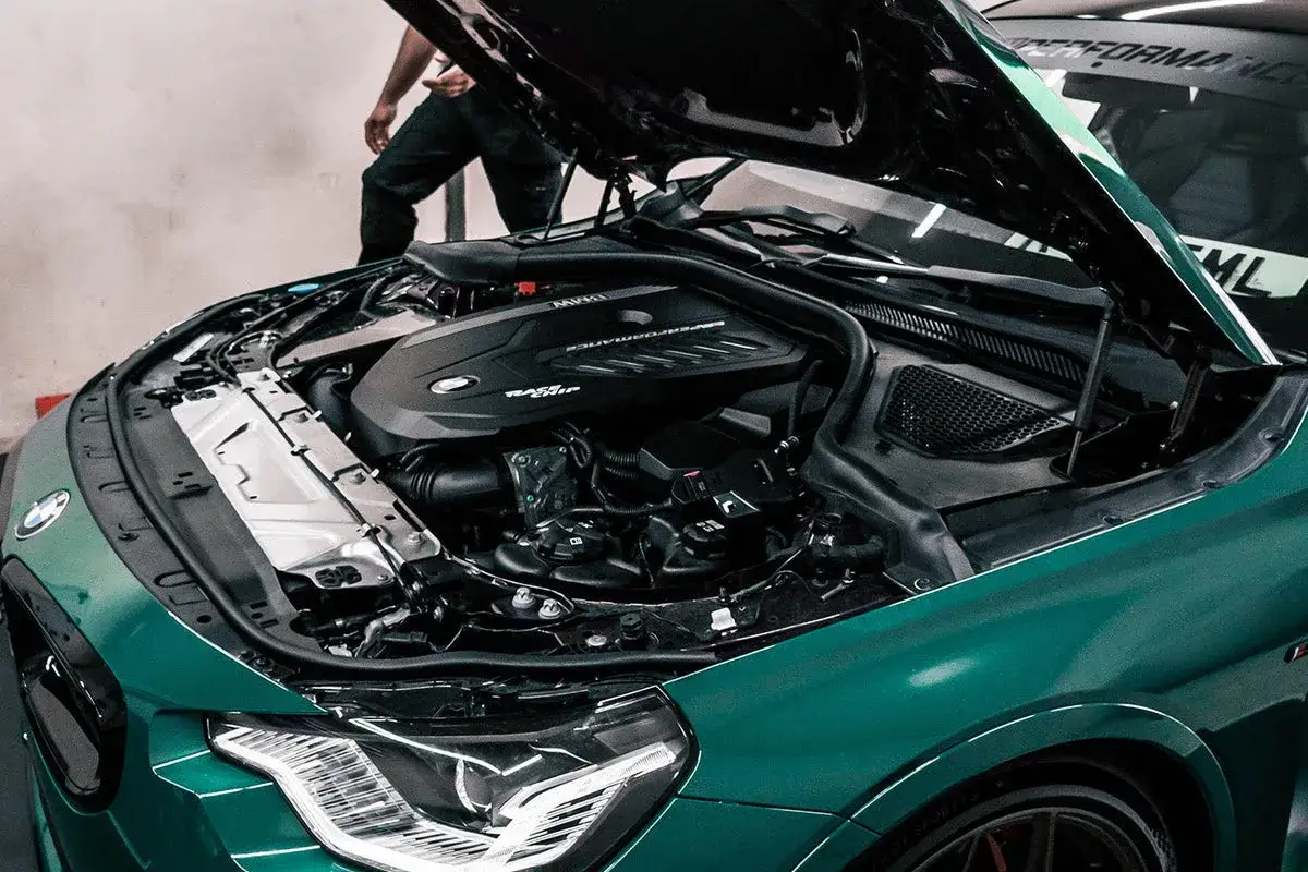 Zielony BMW 140i z otwartą maską, ukazującą potężny silnik M Performance.