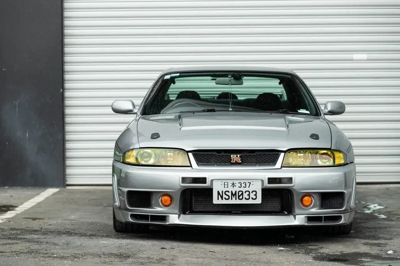 Srebrne r33 GT-R z żółtymi światłami i tablicą NSM033, gotowe do jazdy.