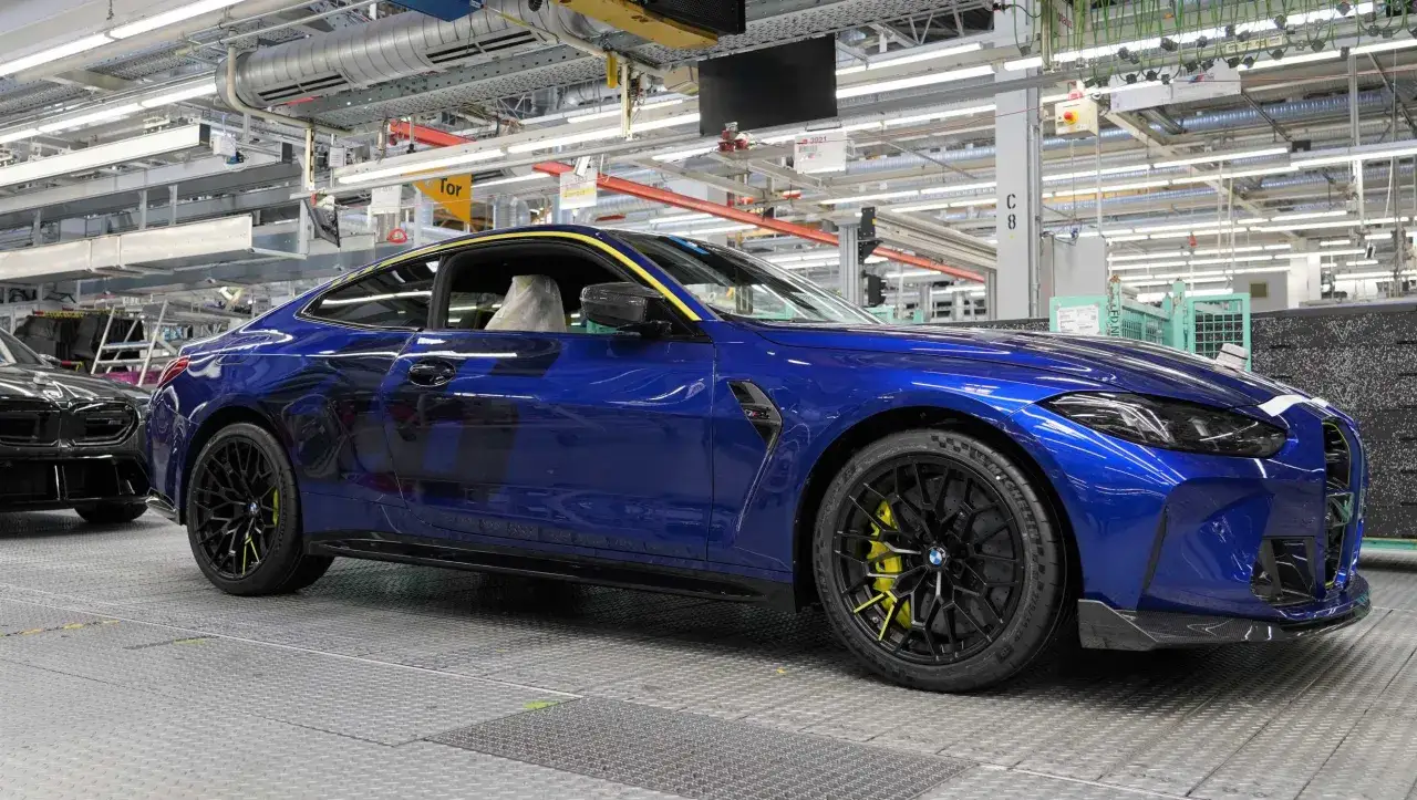 Błękitne BMW M4 CS z żółtymi akcentami na felgach i zaciskach hamulcowych, gotowe do opuszczenia linii produkcyjnej.