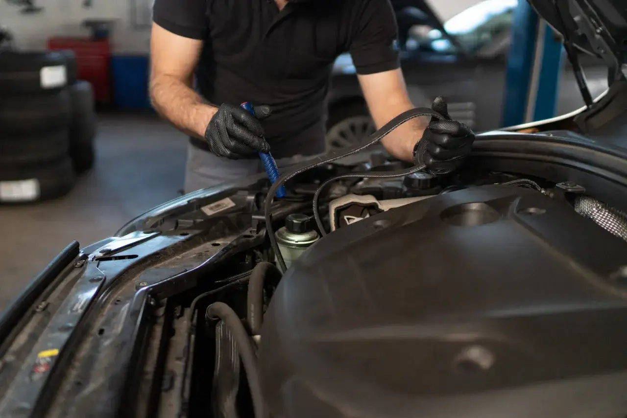 Mechanik w czarnych rękawiczkach wymienia pasek rozrządu w samochodzie.