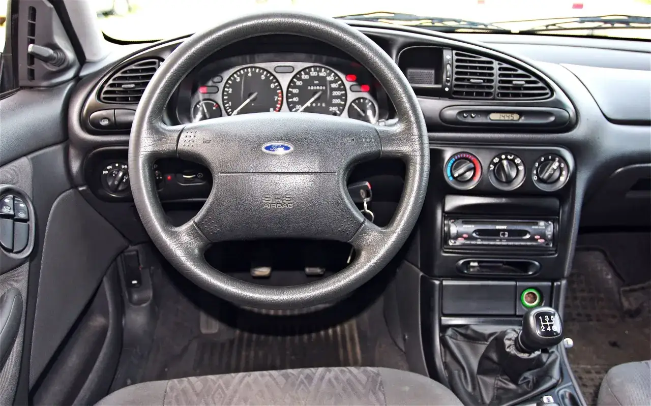 Wnętrze Ford Mondeo MK2: kierownica z logo Ford, deska rozdzielcza z zegarami, radio i nawiewy.