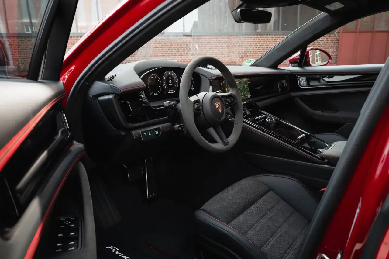 Wnętrze czerwonego Porsche Panamera GTS z czarną tapicerką i czerwonymi przeszyciami. Widoczna kierownica, deska rozdzielcza i siedzenie.