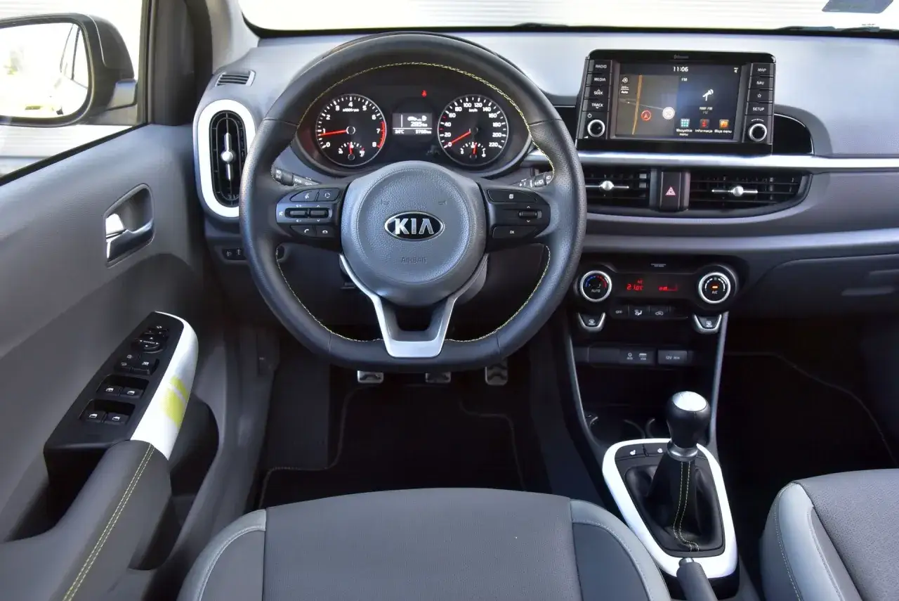 Wnętrze Kia Picanto, kierownica z żółtymi przeszyciami i ekranem multimedialnym. Wiele osób szuka kia picanto opinie, by poznać ten model.