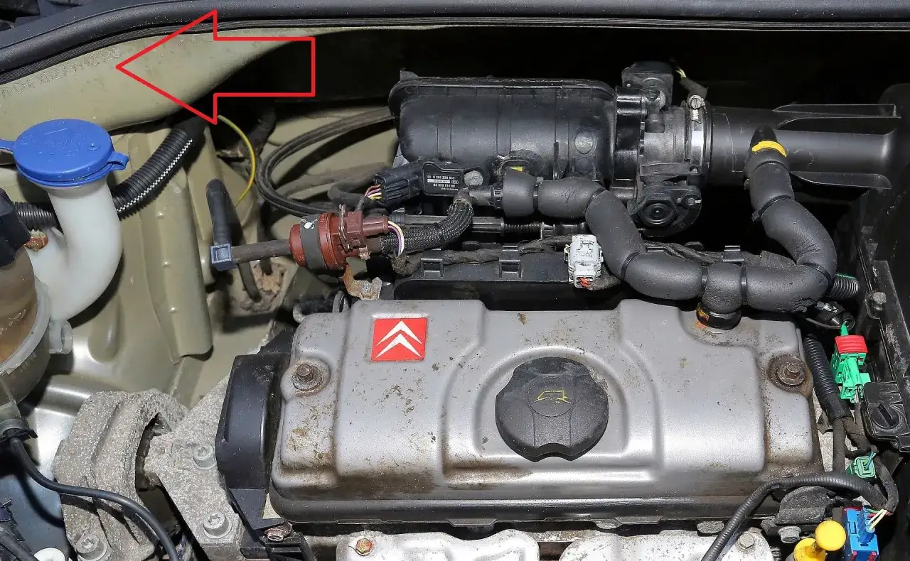 Silnik Citroen C3 2003. Widoczny jest fragment silnika z osprzętem, w tym pokrywa zaworów z logo Citroen. Czerwona strzałka wskazuje na numer VIN.