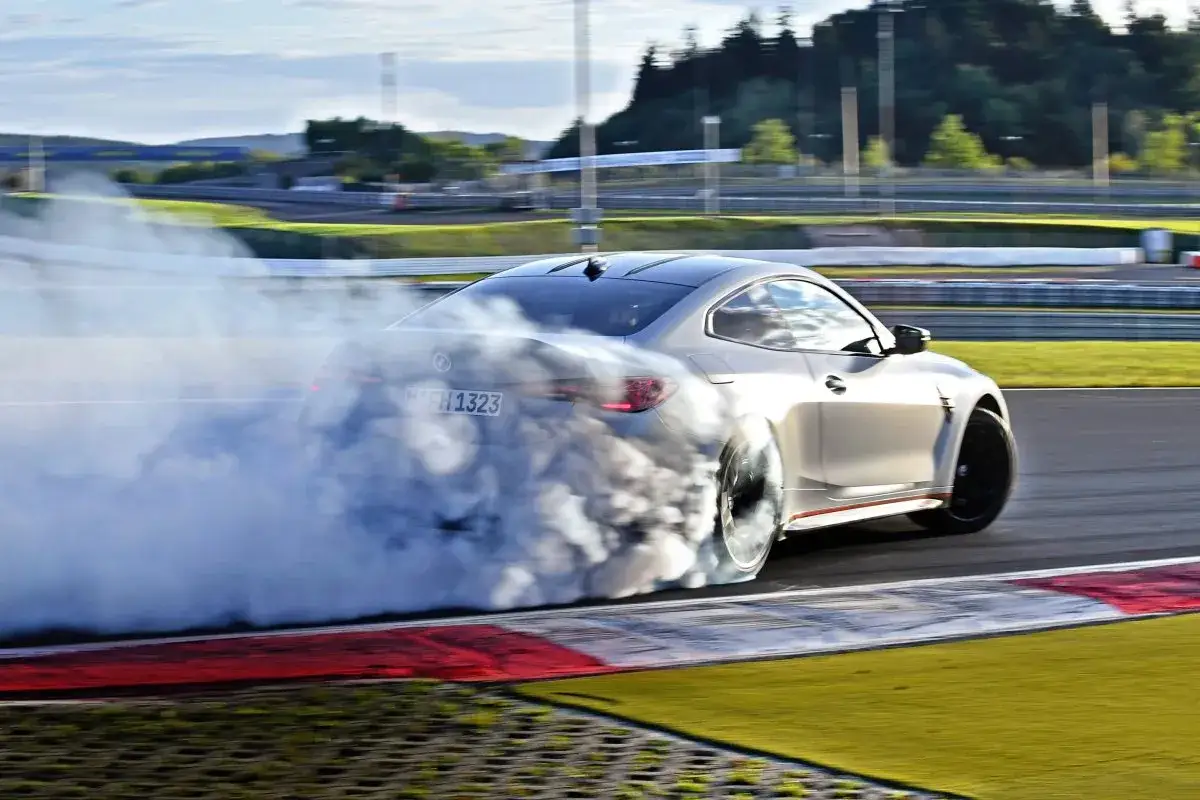 Srebrne BMW M4 CSL na torze wyścigowym, wykonujące efektowny drift, otoczone gęstym dymem z opon.
