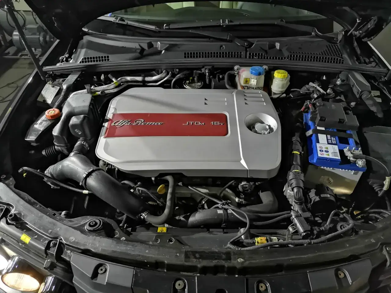 Silnik Alfa Romeo 159 1.9 JTD z widocznym osprzętem i akumulatorem.