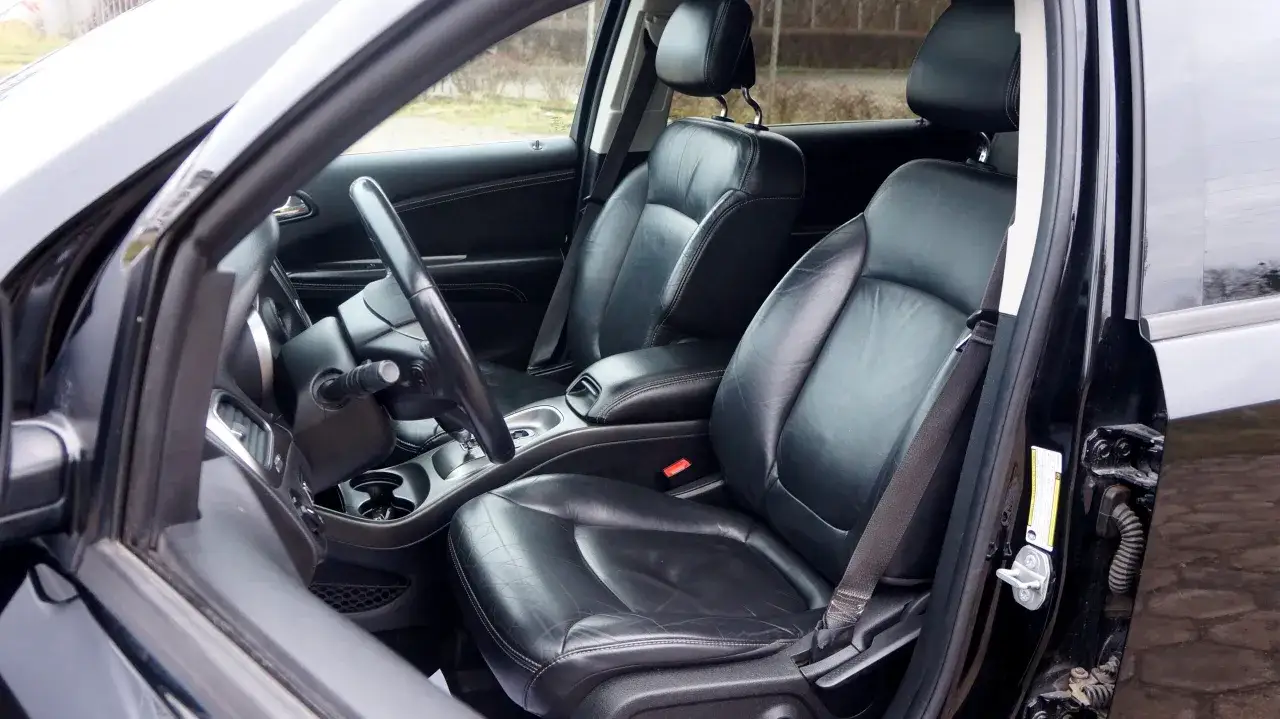 Wnętrze Dodge Journey 3.6 z czarną skórzaną tapicerką, widok na przednie fotele i deskę rozdzielczą.