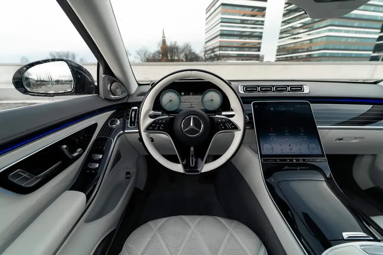 Wnętrze Maybach S580: biała kierownica, duży ekran, pikowane fotele i eleganckie detale tworzą luksusową atmosferę.