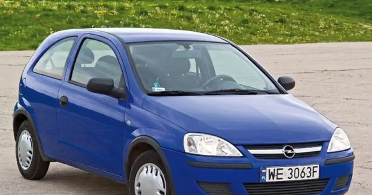 Niebieski Opel Corsa C 1.2 z tablicą rejestracyjną WE 3063F stoi na tle zielonej trawy.