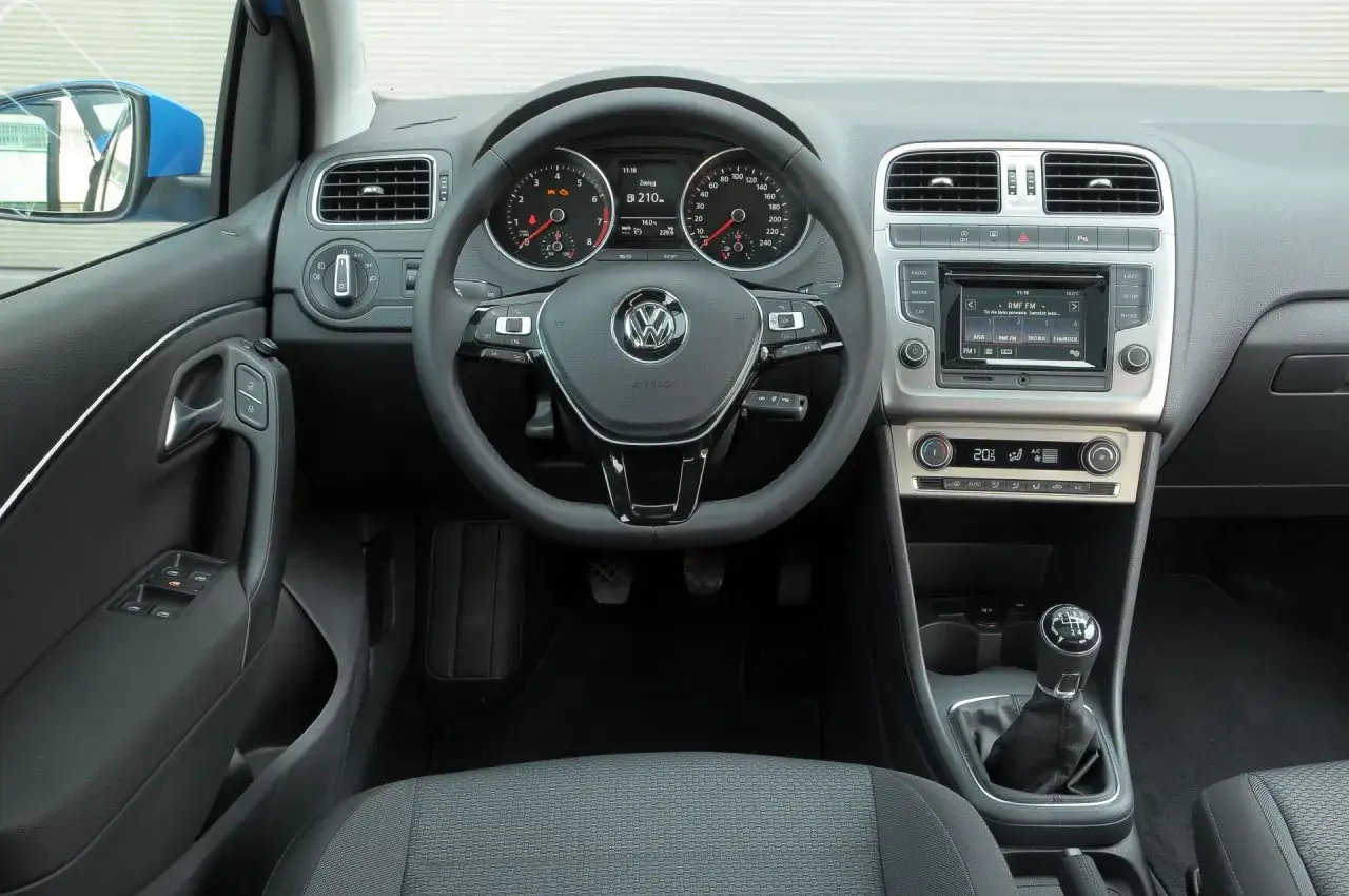 Wnętrze Volkswagena Polo 6: kierownica z przyciskami, deska rozdzielcza z radiem i klimatyzacją, dźwignia zmiany biegów.