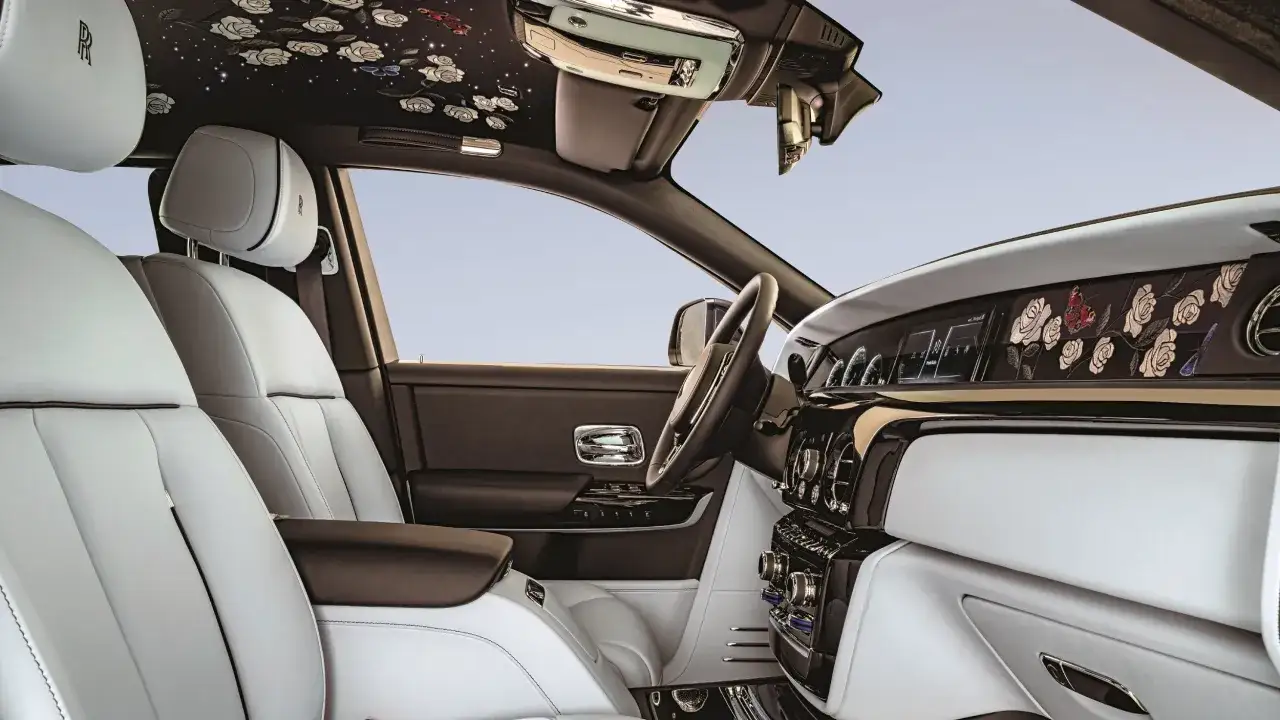 Wnętrze Rolls-Royce Phantom z białymi skórzanymi fotelami i podsufitką ozdobioną kwiatami. Poznaj Rolls-Royce Phantom cena i luksus.