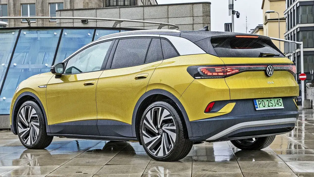 Żółty Volkswagen ID.4 z czarnymi akcentami i srebrnym dachem, zaparkowany na mokrej, miejskiej nawierzchni.