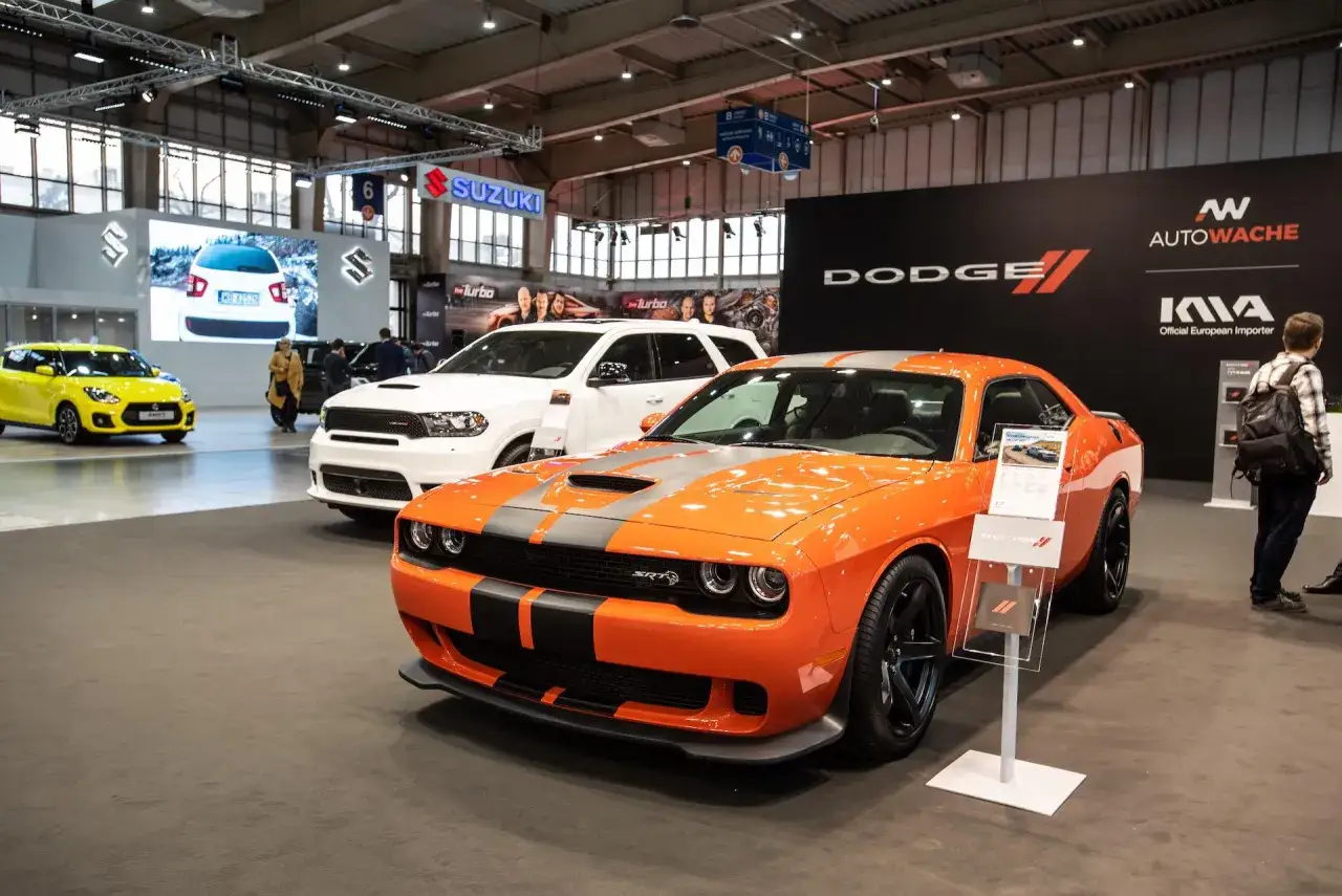 Pomarańczowy Dodge Challenger SRT na wystawie. Sprawdź dodge challenger cena i specyfikację. Obok biały Dodge Durango.
