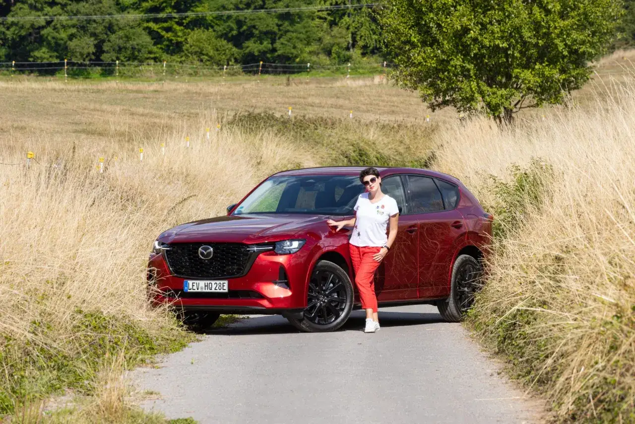 Kobieta w czerwonych spodniach stoi obok czerwonej Mazdy CX-60. Poznaj jej imponujące mazda cx 60 wymiary.