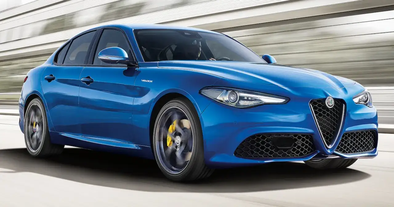 Błękitne Alfa Romeo Giulia Q4 Veloce pędzi po drodze, z widocznym kierowcą i żółtymi zaciskami hamulcowymi.