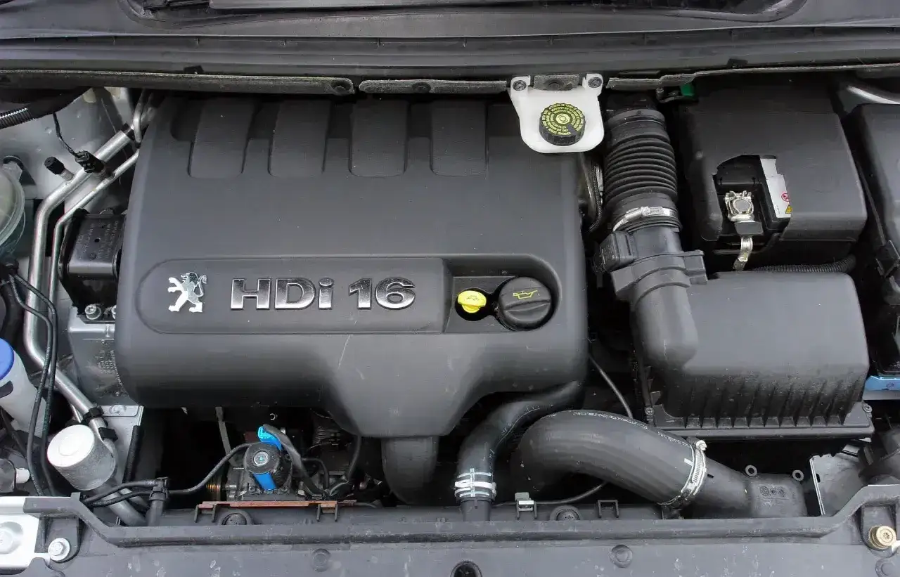 Silnik Peugeot 307 1.6 HDI. Widoczny czarny plastikowy dekiel z logo Peugeot i napisem HDI 16. Obok korek wlewu oleju.