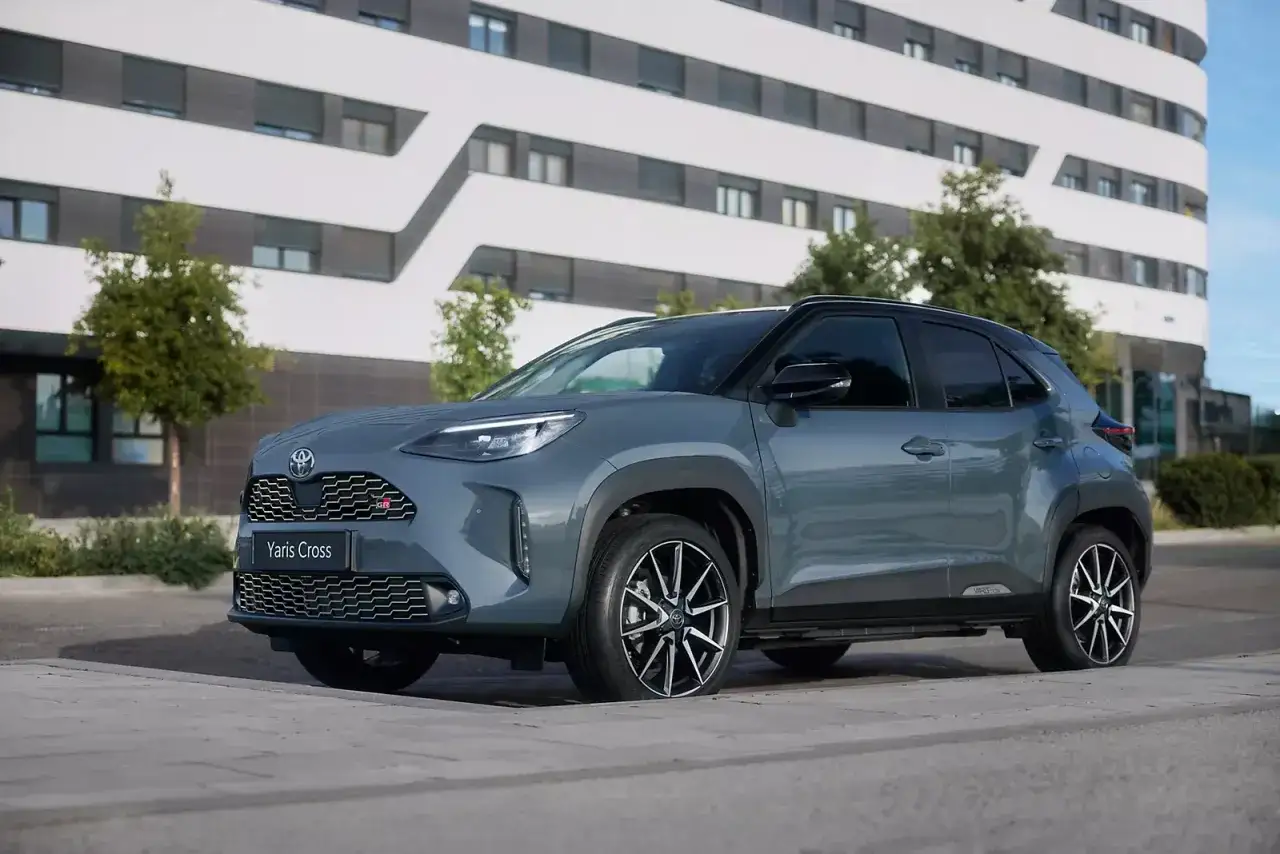 Szary Toyota Yaris Cross 2025 z czarnym dachem, zaparkowany przed nowoczesnym budynkiem.