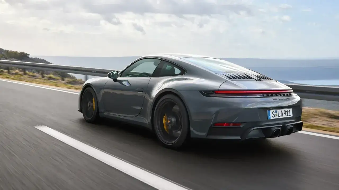 Szary Porsche GTS pędzi po krętej drodze nad morzem.