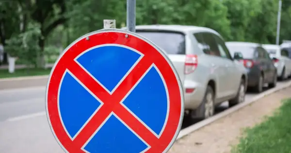 Znak zakazu zatrzymywania się b36. Samochody stoją w rzędzie przy ulicy, ale ten znak przypomina, że nie wolno tu parkować.