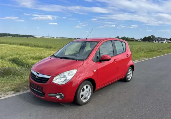 Czerwony Opel Agila 1.2 na tle zielonych pól i błękitnego nieba.